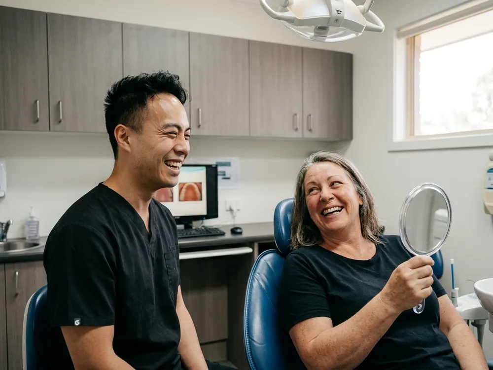 A patient laughing with her dentist while looking at her new smile in a hand mirror.